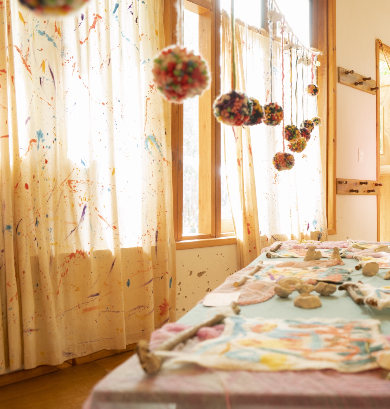 Aula Waldorf con cortinas pintadas, colgantes artesanales y luz natural