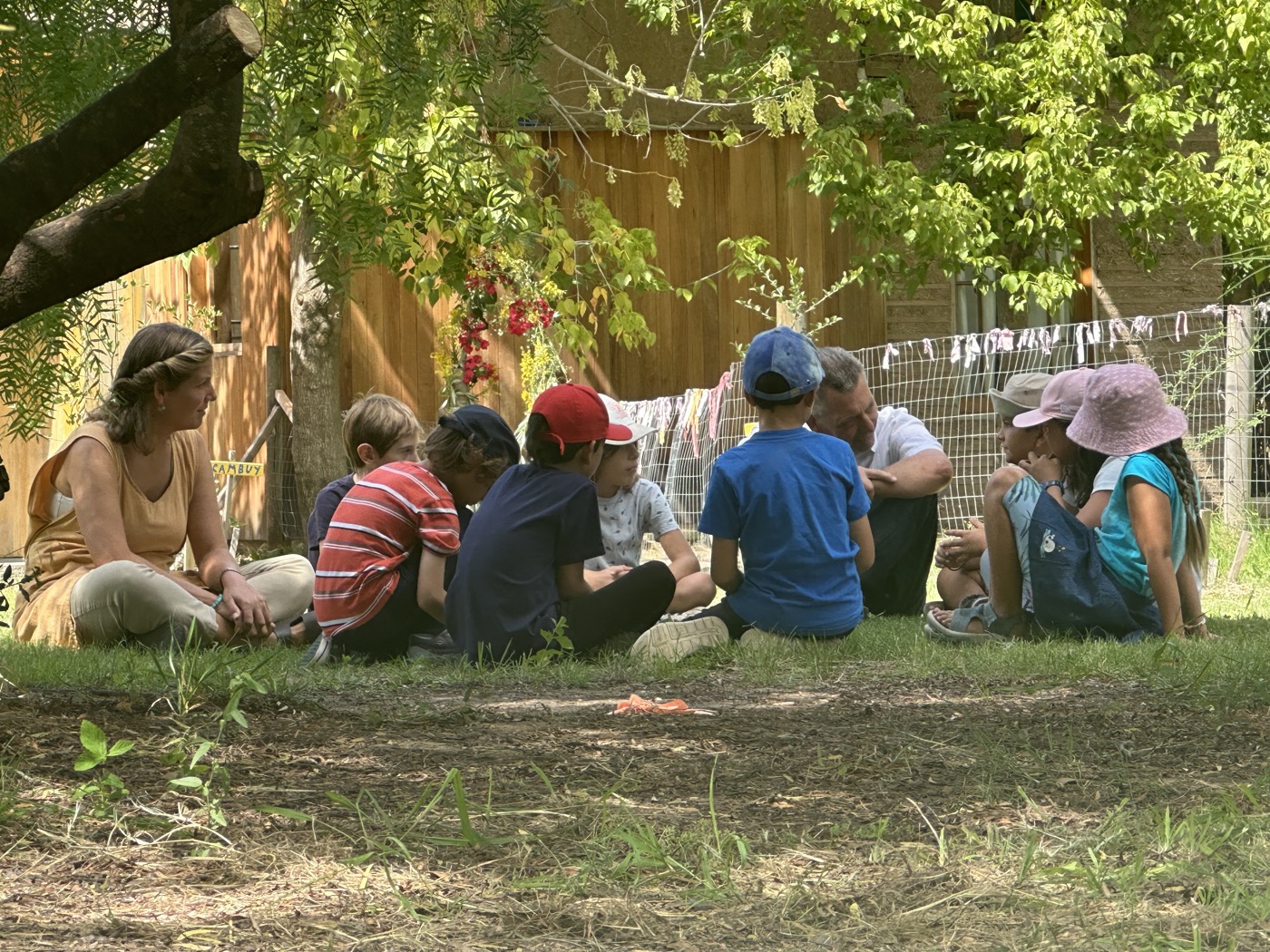 Maestra con grupo de niños en clase al aire libre bajo los árboles